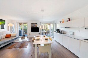 Eine moderne Küche mit weißen Schränken, einem Esstisch für vier Personen und einem Sofa mit Kuhfellteppich.