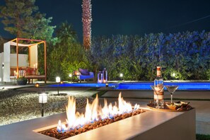 A fire feature with a bar area, outdoor seating, and a pool in the background. - Bermuda Dunes Desert Oasis, Pool & Games (Bermuda Dunes)