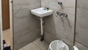 A bathroom with a white sink, a mirror, a shower, and a toilet. - Hotel Minati Palace (Puri)