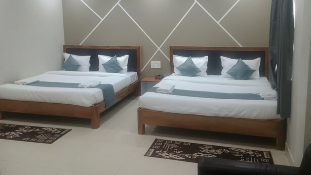 A hotel room with two single beds, each with a wooden headboard, white bedding, and blue pillows. There are ceiling fans, a window with curtains, and a small bedside table with a lamp. - Hotel Minati Palace (Puri)