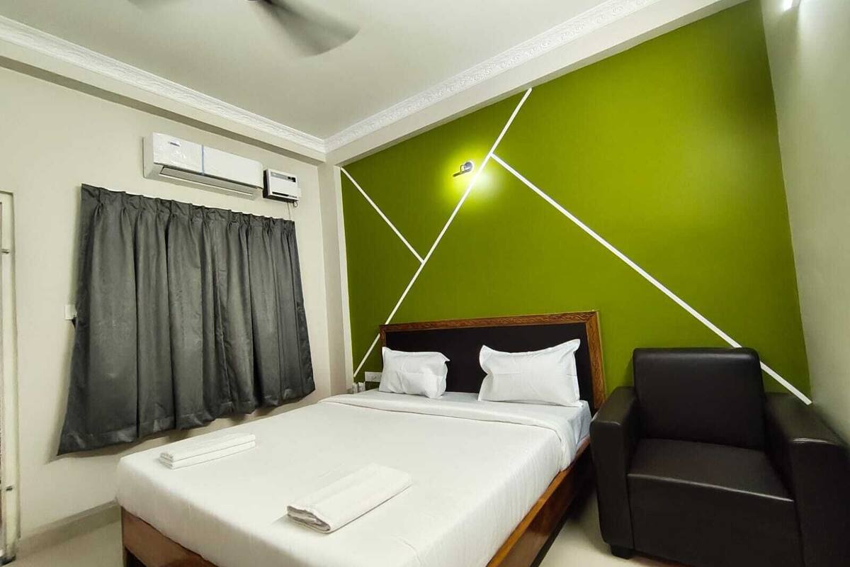 A hotel room with a bed, a chair, a ceiling fan, and a wall with geometric lighting.