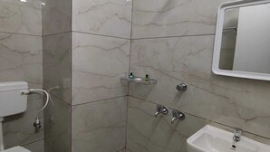 A bathroom with a toilet, sink, shower, and a small trash bin. - Hotel Minati Palace (Puri)