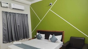 A neatly made bed with a wooden headboard, grey curtains, and a grey chair. - Hotel Minati Palace (Puri)