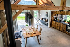 A dining area with a wooden table set for a meal, a sofa in the background, and a kitchen with wooden cabinets and a stove. - Modern converted barn with whirlpool in beautiful natural surroundings (Gutach (Schwarzwaldbahn))