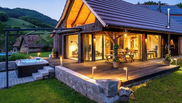 A wooden cabin with a deck, outdoor seating, and a hot tub.