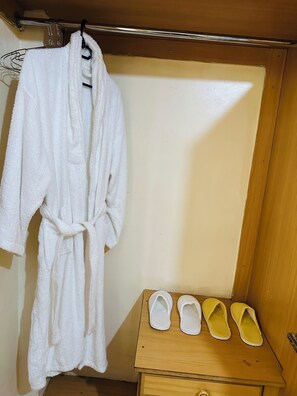 A bathroom with a white bathrobe hanging on a metal rack, a wooden vanity with three pairs of slippers, and a wooden door. - Stylish 1BR retreat in TRM Drive, Nairobi with modern comfort and serene vibes. (Nairobi)