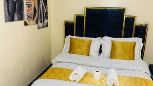 Ein ordentlich bezogenes Bett mit Gold- und Weißtönen, ein Kopfteil mit goldener Zierleiste und zwei Handtücher auf dem Bett.