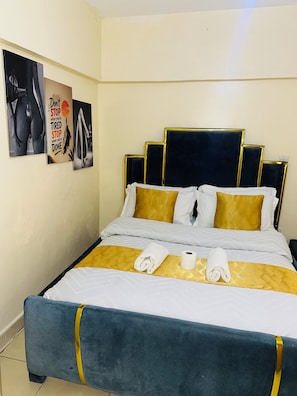 A neatly made bed with a gold and white color scheme, a headboard with gold trim, and two towels on the bed. - Stylish 1BR retreat in TRM Drive, Nairobi with modern comfort and serene vibes. (Nairobi)
