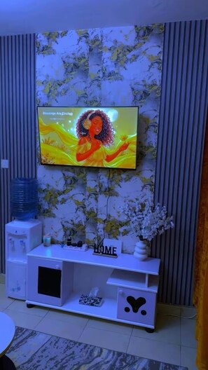 A television mounted on a wall with a floral wallpaper design. - Stylish 1BR retreat in TRM Drive, Nairobi with modern comfort and serene vibes. (Nairobi)