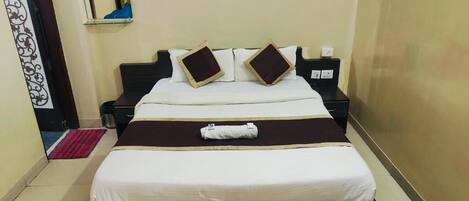 A neatly made bed with a white and brown color scheme, a small bedside table with a lamp, and a wall-mounted mirror.