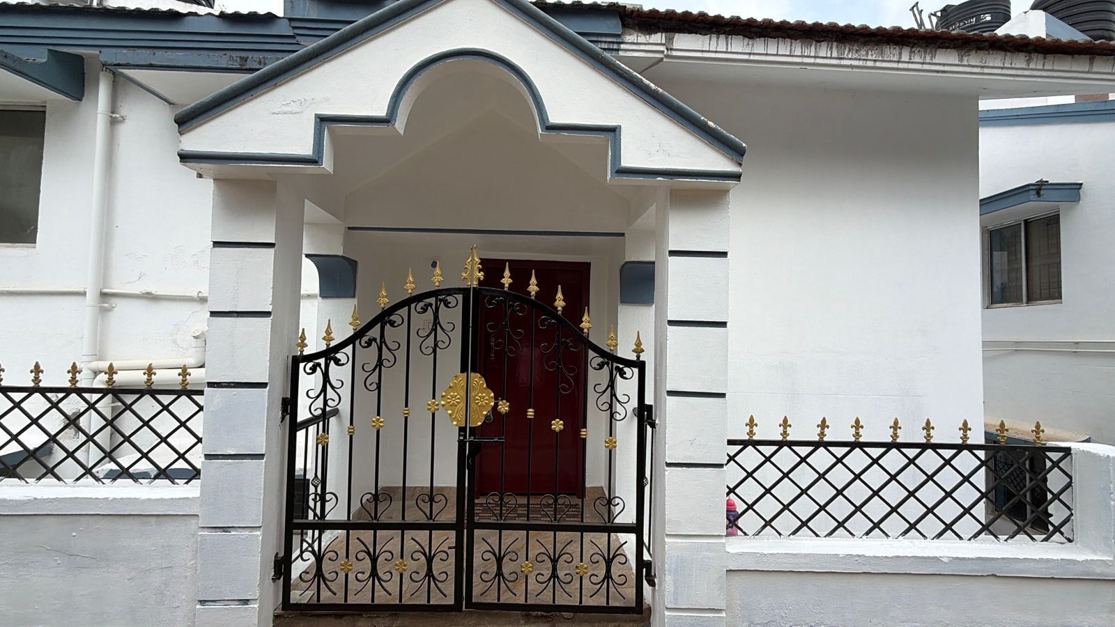 A building with a white facade, a black metal gate with gold accents, and a red door.
