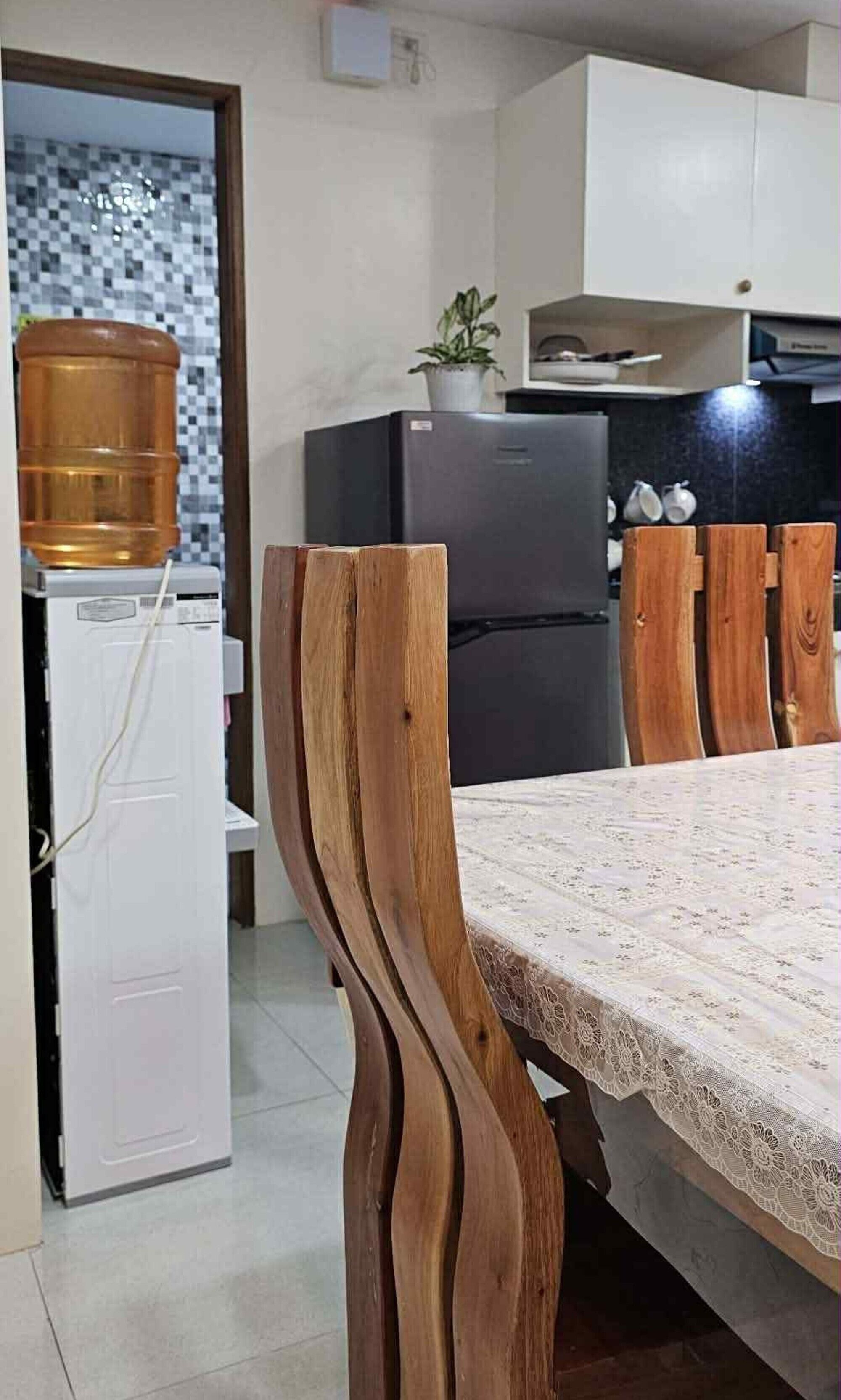 A modern kitchen with a refrigerator, a coffee machine, and a dining table with a lace tablecloth.