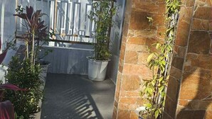 A covered outdoor area with potted plants, a metal fence, and a stone wall. - MEEK'S VILLAS TRANSIENT HOUSE (Baguio)