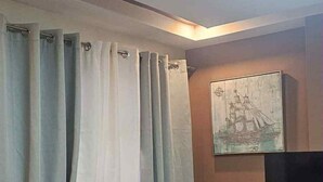 A wooden bench and table in a room with a curtain and a painting on the wall. - MEEK'S VILLAS TRANSIENT HOUSE (Baguio)