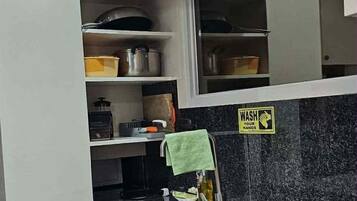 A kitchen with a granite countertop, stainless steel sink, and cabinets with wooden handles. There is a 'WASH YOUR HANDS' sign on the wall.