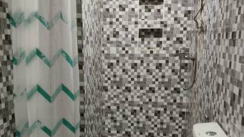 Un bagno con parete rivestita di piastrelle a scacchi, doccia dotata di rubinetto curvo e WC con piccola finestra.