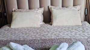 Cama bem arrumada com cabeceira, duas almofadas e uma caixa de boas-vindas em carpete texturizado.
