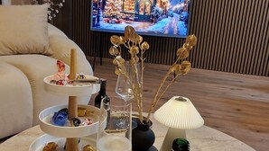 Uma mesa redonda com uma garrafa de Henkell Piccolo, um copo de vinho branco, um vaso com galhos secos e uma bandeja com chocolates e uma pequena réplica da Torre Eiffel.