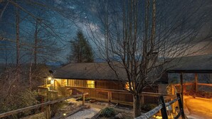 Ein rustikales Holzhaus mit einer Laube, umgeben von einem eingezäunten Garten und einem hölzernen Weg zum Eingang.