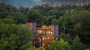 Um edifício moderno de vários andares rodeado por floresta densa, com varandas visíveis e grandes janelas.