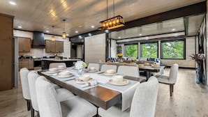 Cozinha moderna com armários de madeira, área de jantar com uma mesa grande posta para seis pessoas e amplas janelas que proporcionam iluminação natural.