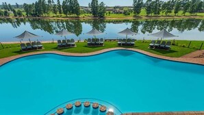 A swimming pool with lounge chairs and umbrellas, surrounded by a brick deck and a view of a lake and greenery. - Pine Lake Resort (White River)