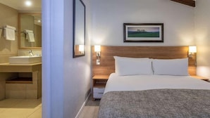 A hotel room with a bed, a nightstand, a wall-mounted picture, and a bathroom with a sink and mirror. - Pine Lake Resort (White River)