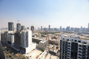 A high-rise building with multiple floors, a parking area, and a construction site with cranes. - Bloomfields Cozy Stu Binghatti (Dubai)