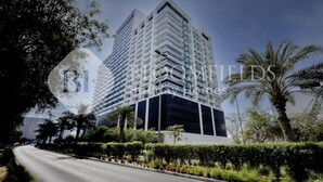 A modern high-rise building with a glass facade, surrounded by greenery and palm trees. - Bloomfields Cozy Stu Binghatti (Dubai)
