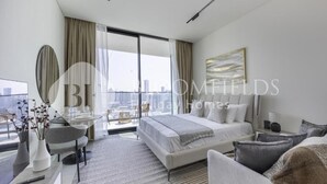 A modern hotel room with a large bed, a desk, a chair, and a view of the city. - Bloomfields Cozy Stu Binghatti (Dubai)