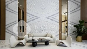 A modern living room with a marble-patterned wall, a sofa, two white chairs, and a coffee table. - Bloomfields Cozy Stu Binghatti (Dubai)
