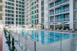 A modern hotel with a large indoor swimming pool, multiple balconies, and sun loungers. - Bloomfields Cozy Stu Binghatti (Dubai)
