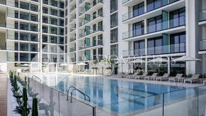 A modern hotel with a large indoor pool, multiple balconies, and sun loungers. - Bloomfields Cozy Stu Binghatti (Dubai)