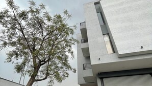 Un edificio moderno con techo plano y un árbol grande en la fachada. Se observa una señalización de hostal y un obturador cerrado.