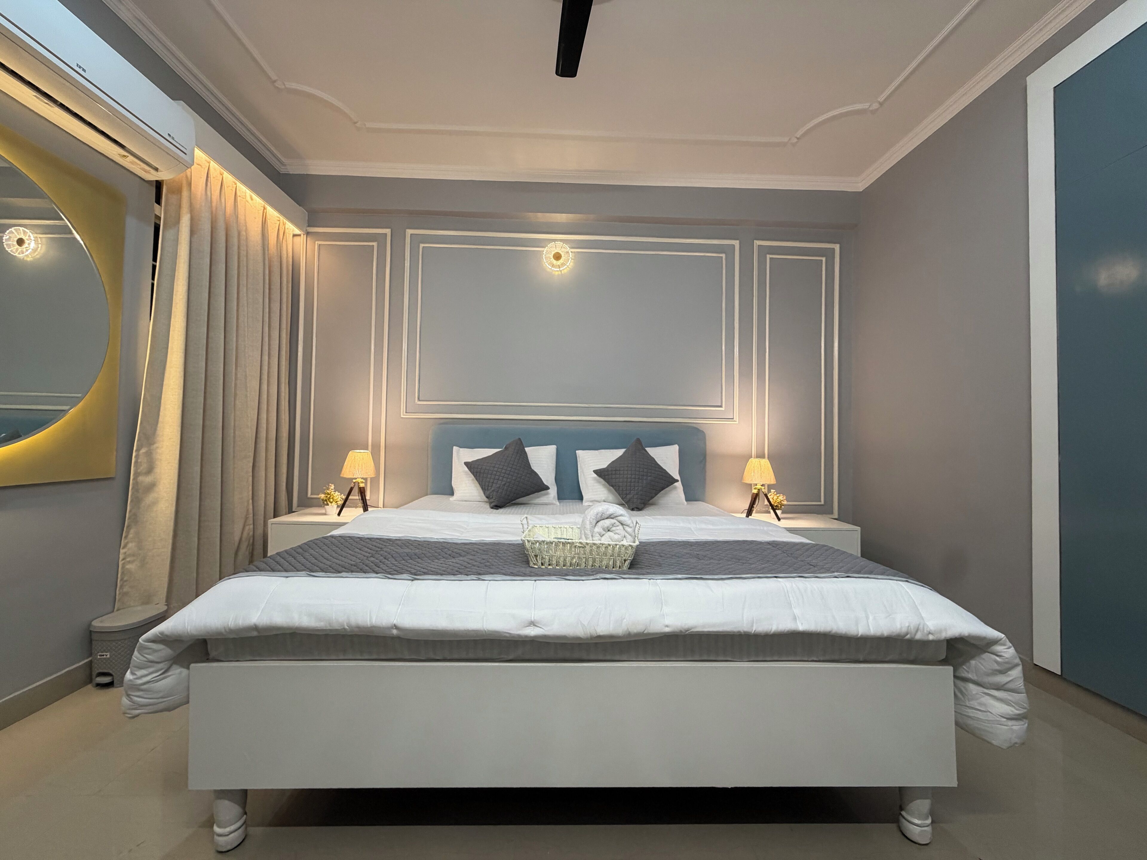 A modern bedroom with a large bed, two bedside tables with lamps, and a wall-mounted air conditioner.