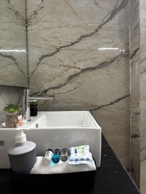 A bathroom with a white sink, marble walls, a mirror, and toiletries on the counter.