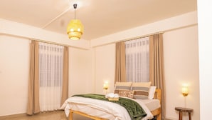Un dormitorio con cama, cortinas, lámpara colgante, mesita de noche y alfombra.
