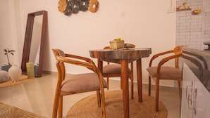 Un comedor con una mesa redonda de madera, dos sillas, un tapete tejido y un adorno en la pared.