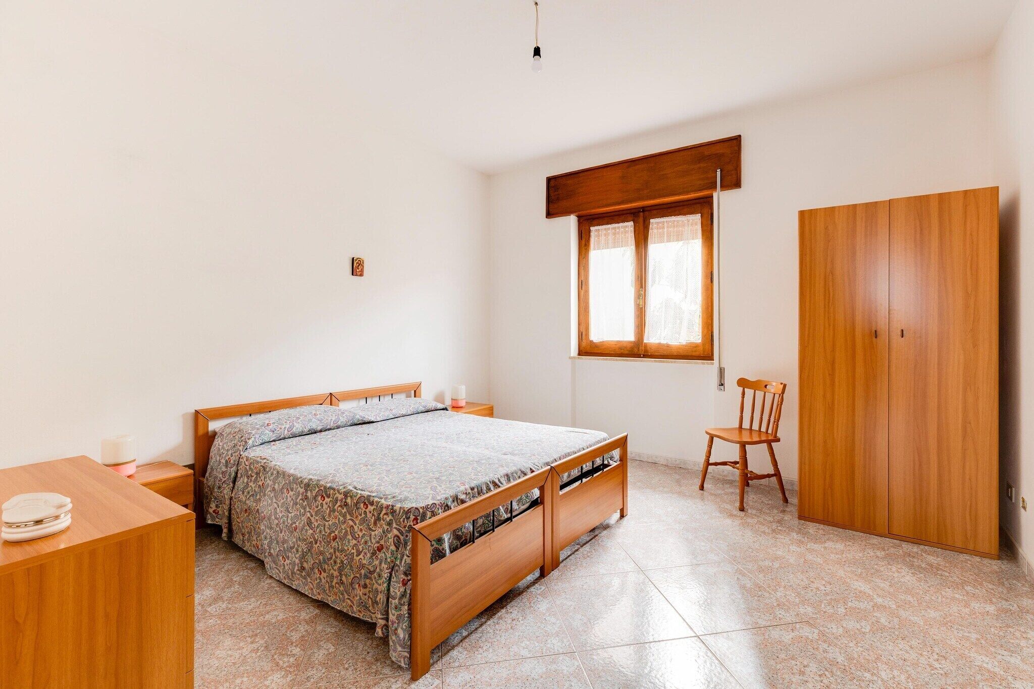 Une chambre à coucher avec un lit en bois, une armoire en bois, une chaise et une petite table de chevet.