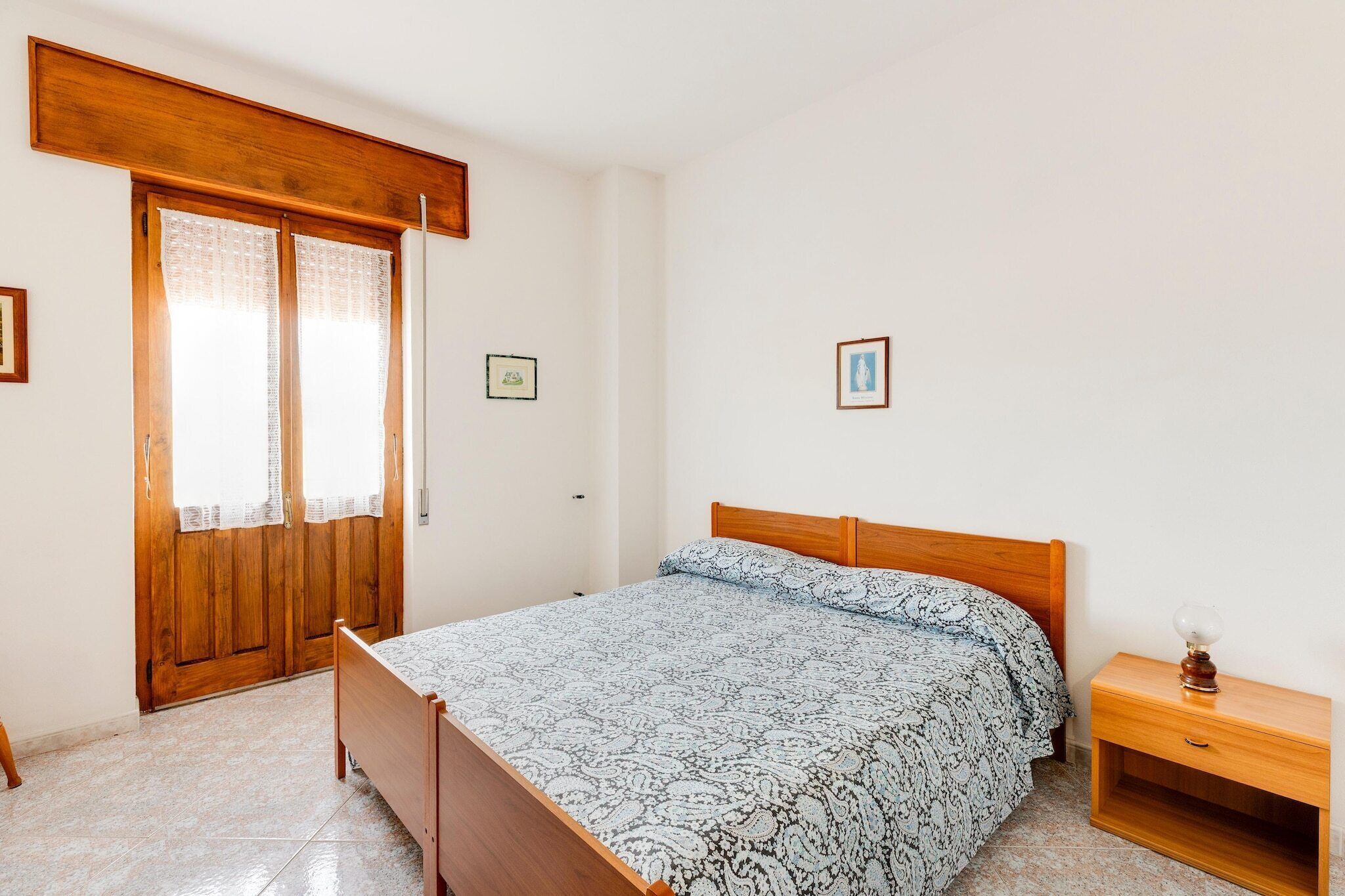 A bedroom with a wooden bed, a nightstand, a wooden wardrobe, and two framed pictures on the wall.