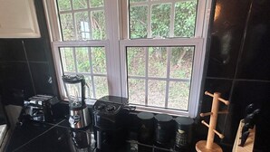 Een keuken met een zwart aanrecht, een blender, een koffiezetapparaat en een raam met uitzicht op groen.