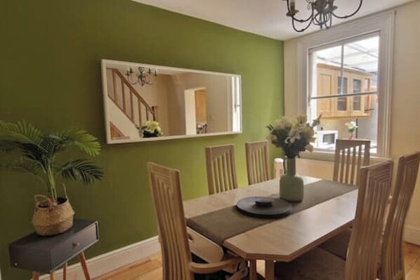 A dining area with a wooden table, chairs, a vase with flowers, and a mirror on the wall. - Windsor Castle Amazing Cottage | 2-Min Walk | Central & Stylish (Windsor)