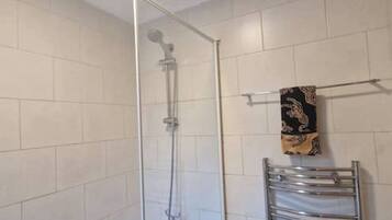 Una ducha con puerta de cristal, un perchero con una toalla estampada y un toallero de metal.