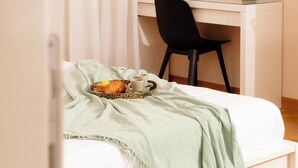 Een slaapkamer met een bed, een bureau, een stoel en een dienblad met eten en drinken.