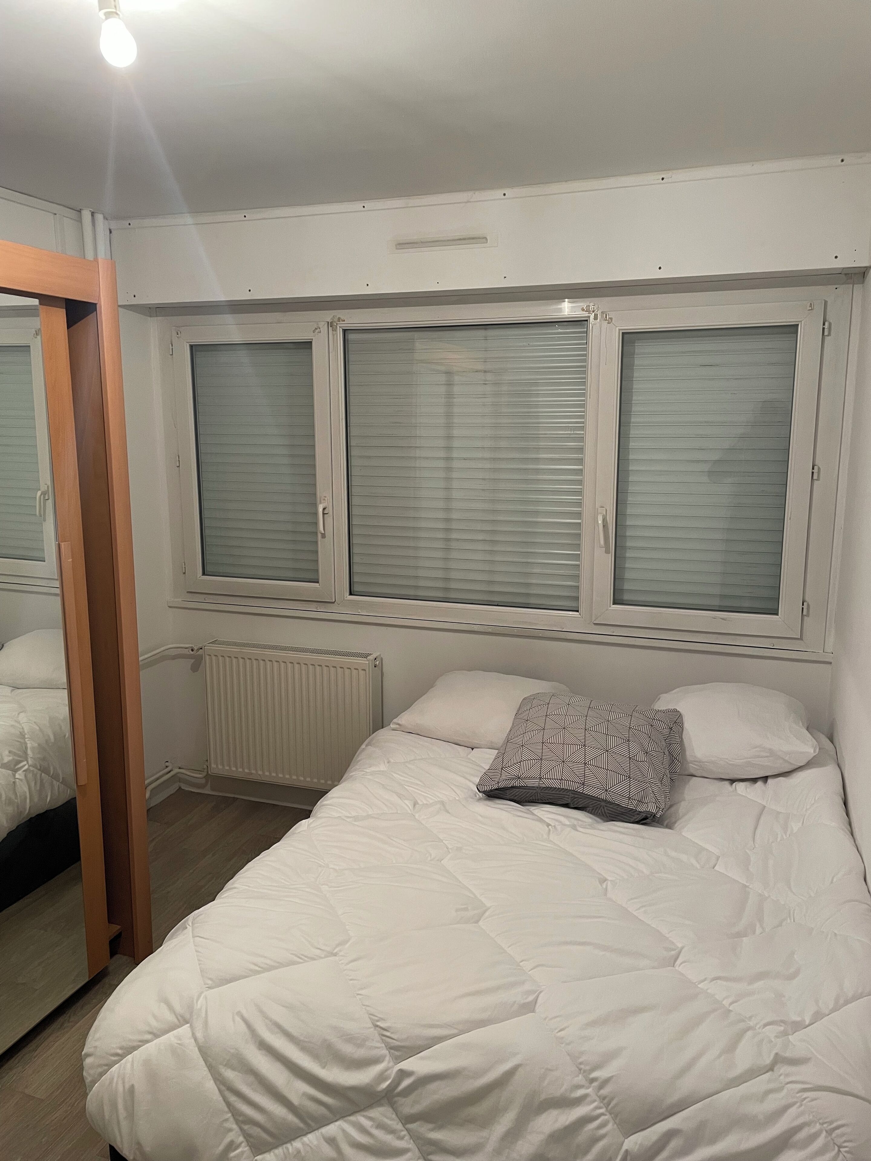 A bedroom with a bed, a radiator, and a window with blinds.