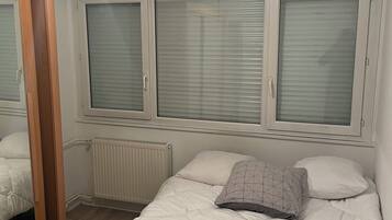 A bedroom with a bed, a radiator, and a window with blinds.