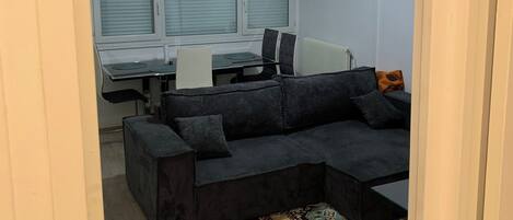 A compact living space with a dark grey sofa, a patterned rug, and a desk with a computer.