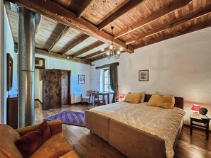 Une chambre à coucher avec un grand lit, des poutres en bois, un radiateur, une table avec des chaises et une fenêtre avec des rideaux.