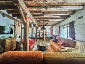 Un intérieur rustique avec des poutres apparentes, un canapé, un téléviseur et une cheminée.