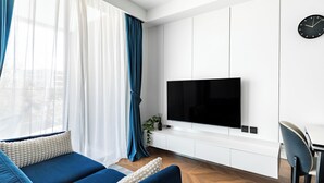 A modern living room with a sofa, a TV mounted on a white wall, and a dining area with a chair. - Sunshine by Villacarte (Choeng Thale)